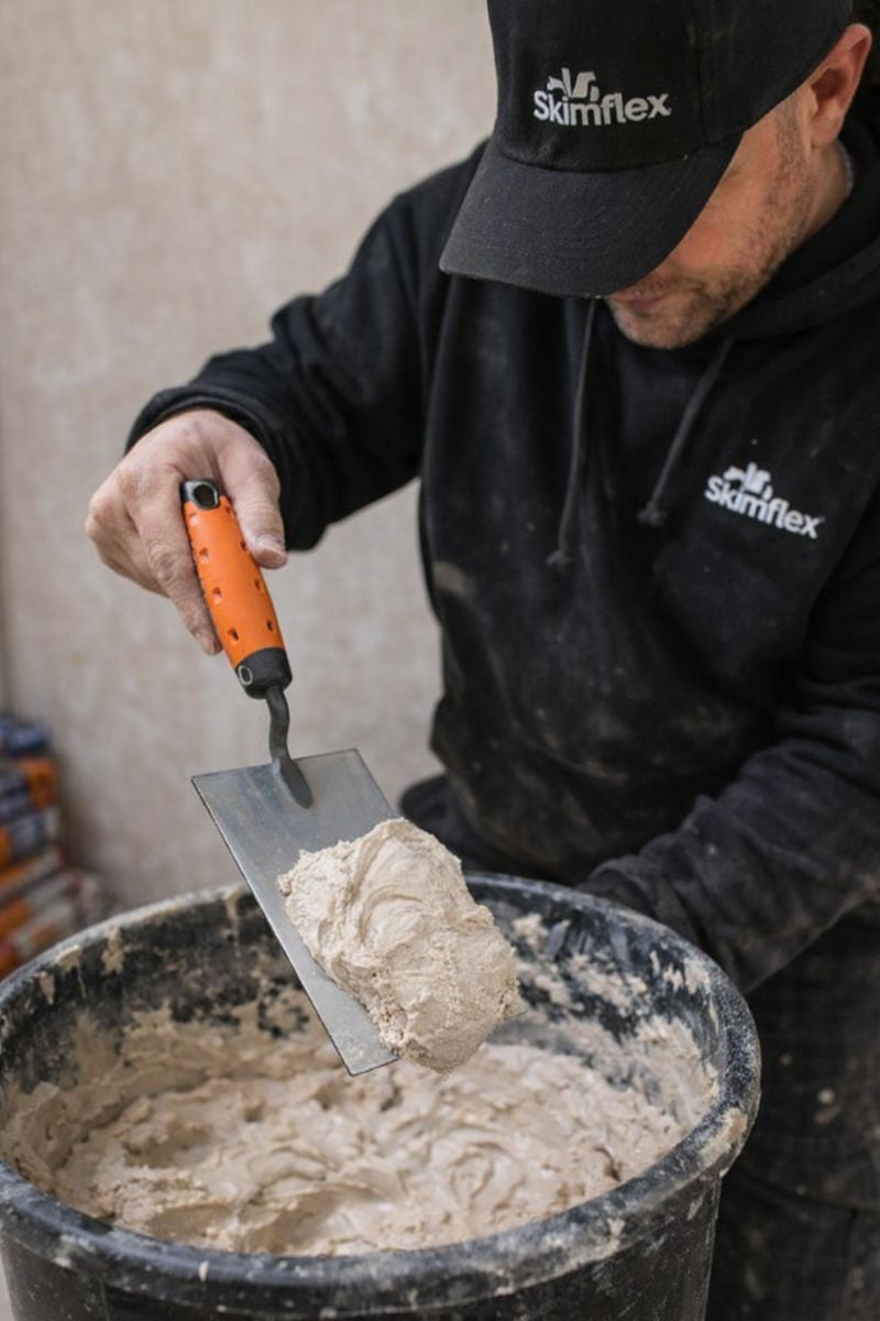 plasterer scooping plaster from bucket with bucket trowel