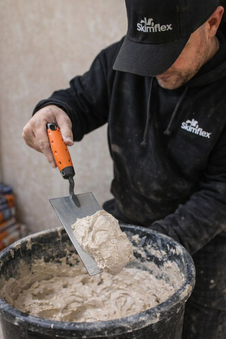 plasterer scooping plaster from bucket with bucket trowel